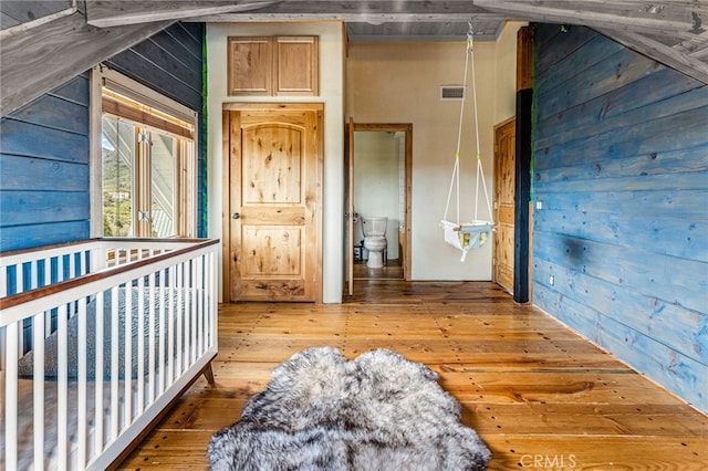 bedroom featuring connected bathroom, wooden walls, and hardwood / wood-style flooring