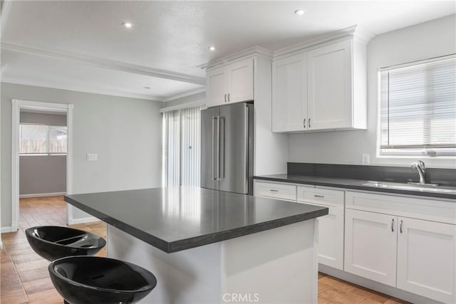 kitchen featuring high end refrigerator, a kitchen island, sink, white cabinetry, and a kitchen breakfast bar