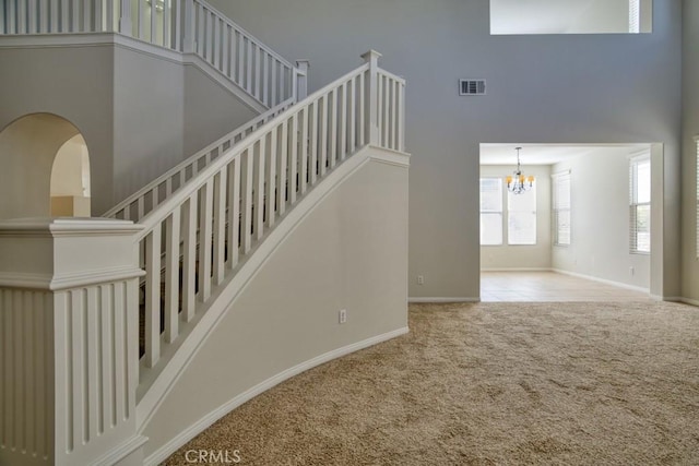 stairway with a high ceiling, carpet floors, and a notable chandelier