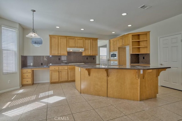 kitchen featuring a center island, light tile patterned flooring, stainless steel microwave, and backsplash