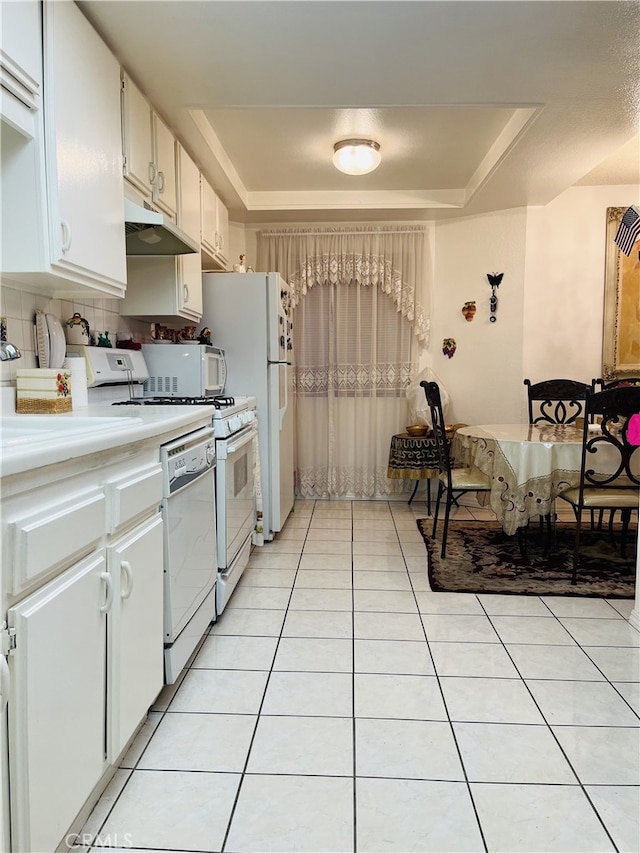 kitchen featuring white cabinets, white appliances, light tile patterned flooring, and a tray ceiling