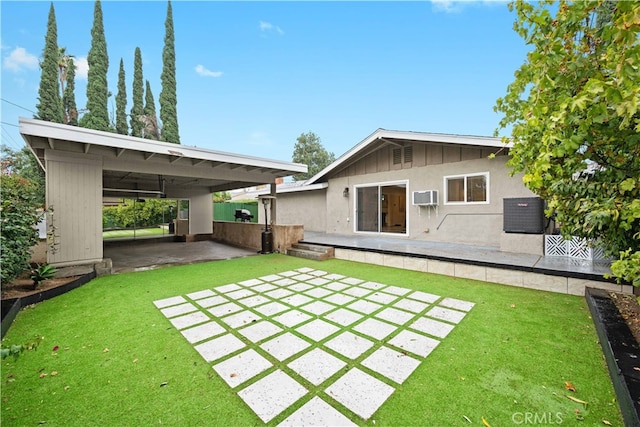 back of house with a wall unit AC, a lawn, and a carport