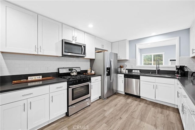 kitchen with appliances with stainless steel finishes, backsplash, sink, light hardwood / wood-style floors, and white cabinetry