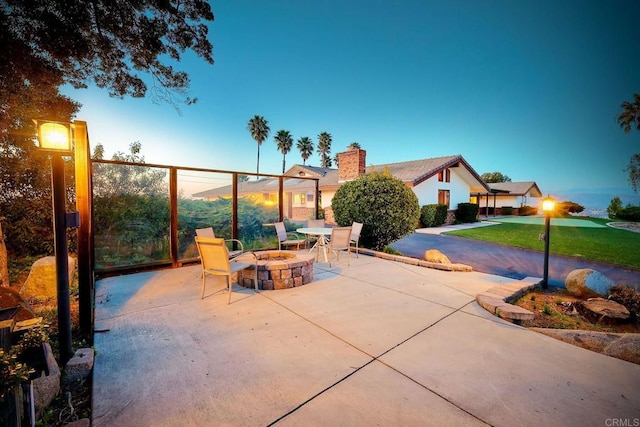 patio terrace at dusk featuring an outdoor fire pit and a lawn