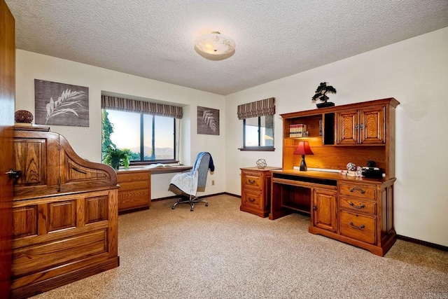 office space with built in desk, a textured ceiling, and light colored carpet