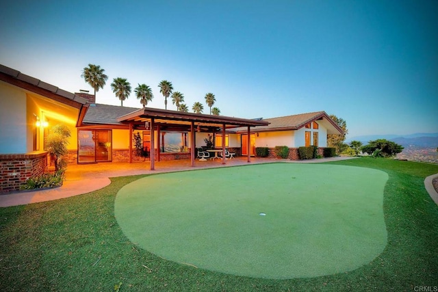 back house at dusk with a patio and a lawn