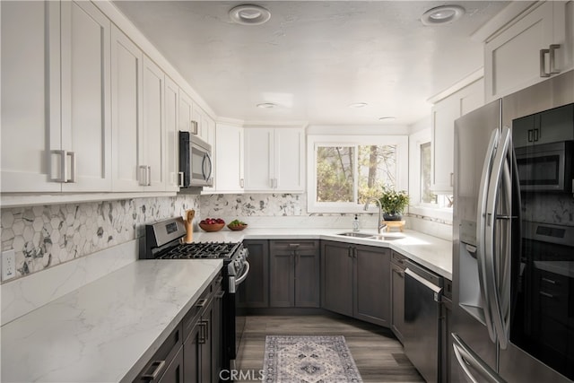 kitchen with tasteful backsplash, light stone counters, hardwood / wood-style flooring, sink, and stainless steel appliances