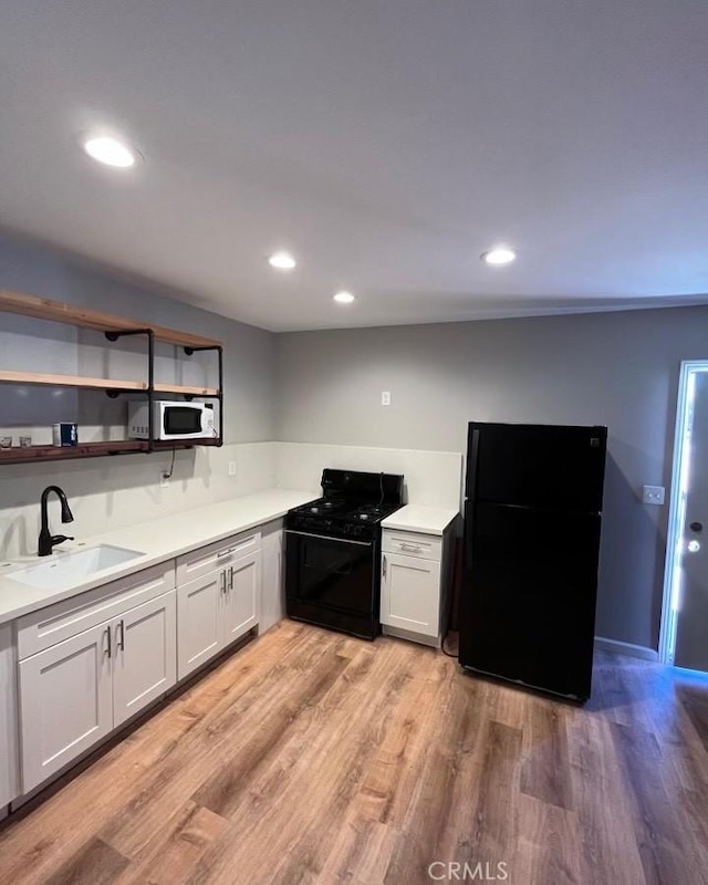 kitchen featuring black appliances, white cabinets, light wood-type flooring, and sink