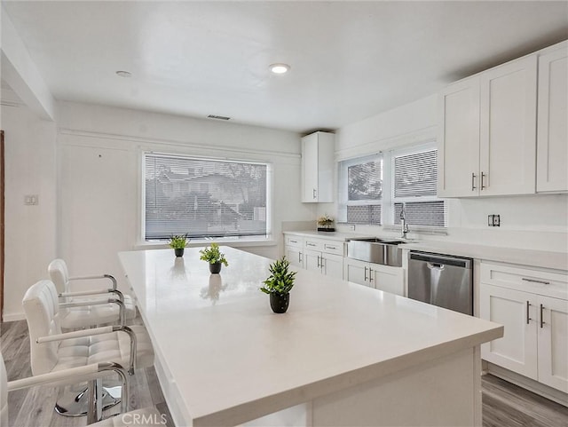 kitchen featuring white cabinetry, a kitchen bar, dishwasher, a kitchen island, and sink