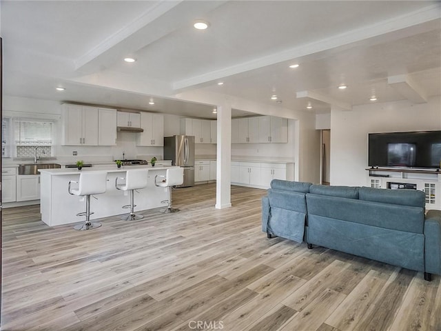 living room with light wood-type flooring, sink, and beamed ceiling