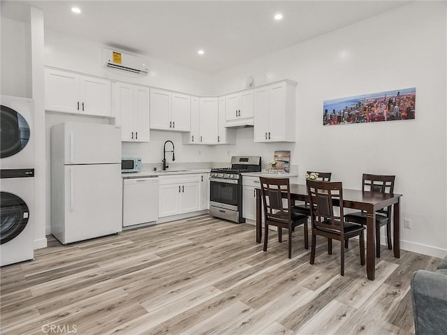 kitchen with white appliances, white cabinetry, stacked washer and dryer, sink, and a wall mounted AC