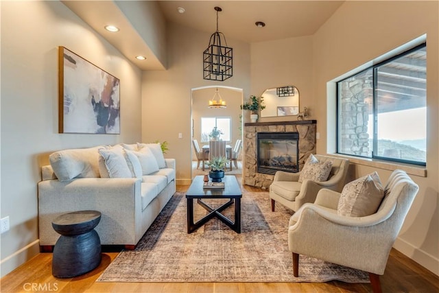 living room with hardwood / wood-style flooring, an inviting chandelier, and a stone fireplace