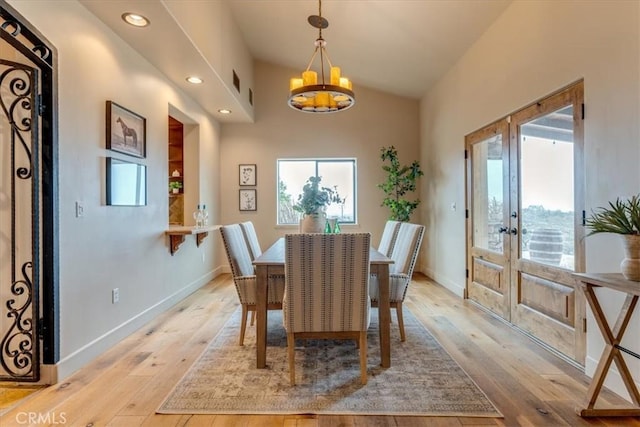 dining area with a chandelier, vaulted ceiling, french doors, and light hardwood / wood-style flooring