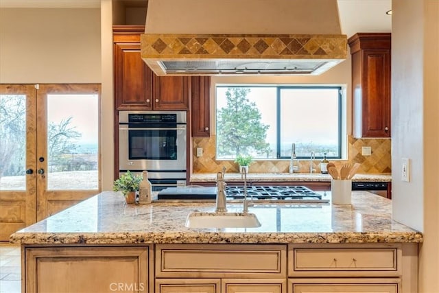 kitchen with stainless steel double oven, backsplash, extractor fan, and light stone counters