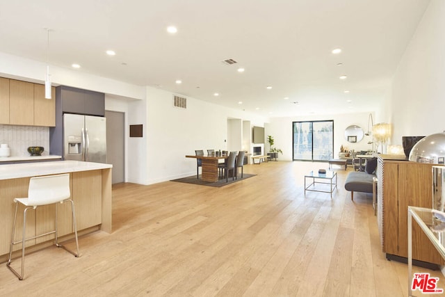 kitchen featuring stainless steel fridge, decorative backsplash, a breakfast bar area, pendant lighting, and light hardwood / wood-style floors