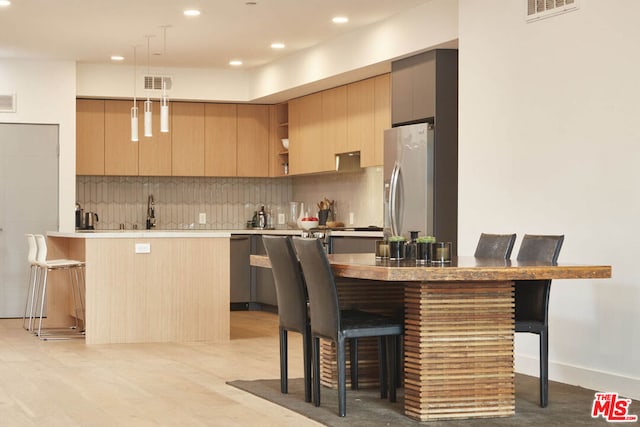 kitchen featuring appliances with stainless steel finishes, pendant lighting, decorative backsplash, a breakfast bar area, and light brown cabinets