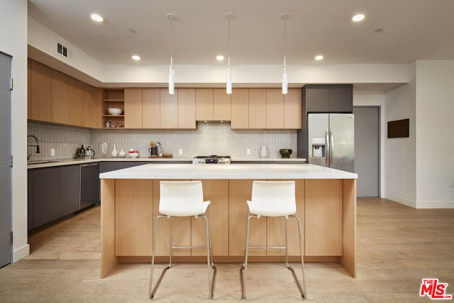 kitchen with appliances with stainless steel finishes, a center island, decorative light fixtures, and light hardwood / wood-style floors