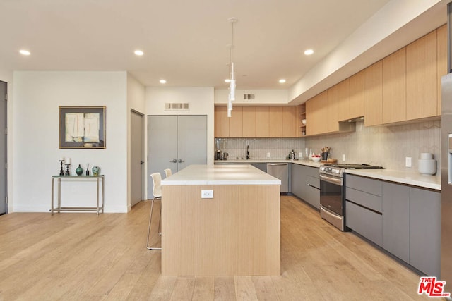 kitchen featuring a center island, light hardwood / wood-style floors, stainless steel appliances, decorative light fixtures, and gray cabinets