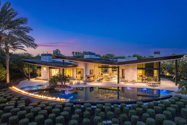 back house at dusk featuring a pool with hot tub and a patio area