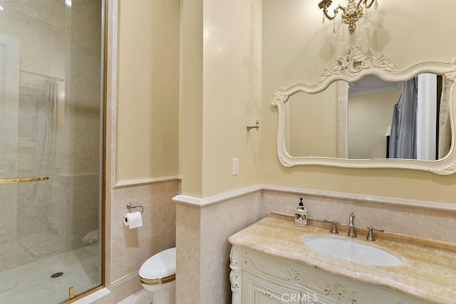 bathroom featuring tile walls, toilet, a stall shower, wainscoting, and vanity