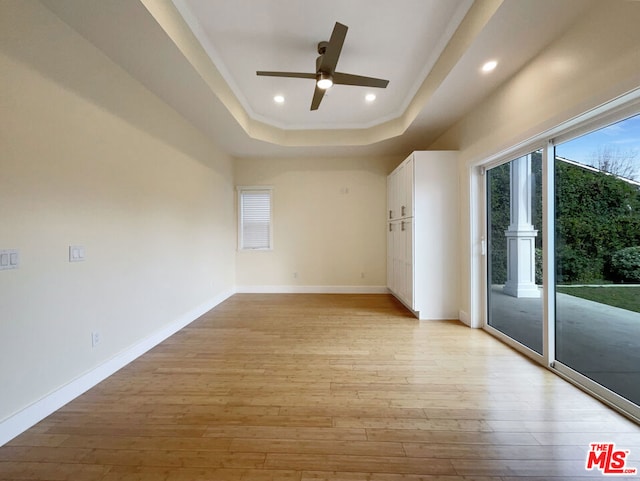 spare room featuring light wood-type flooring, a raised ceiling, and ceiling fan