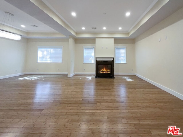 unfurnished living room with wood-type flooring, a tray ceiling, and crown molding