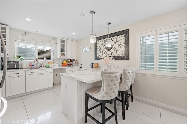 kitchen featuring kitchen peninsula, white cabinets, a kitchen breakfast bar, pendant lighting, and light stone counters