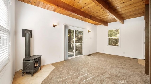 unfurnished living room featuring beamed ceiling, a wood stove, plenty of natural light, and wood ceiling