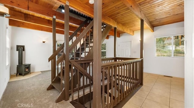 staircase with tile patterned floors, beam ceiling, a wood stove, and wooden ceiling