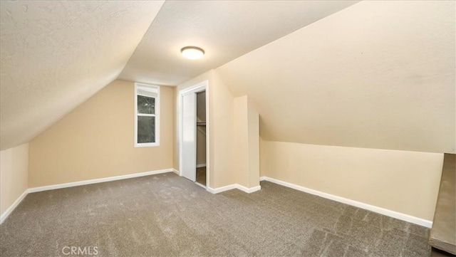 bonus room with dark colored carpet, lofted ceiling, and a textured ceiling