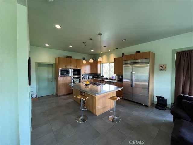 kitchen featuring a kitchen island, decorative light fixtures, built in appliances, light stone counters, and a breakfast bar area