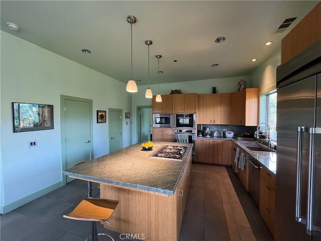 kitchen with decorative light fixtures, a center island, a kitchen bar, sink, and stainless steel appliances