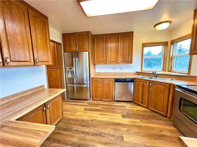 kitchen with stainless steel appliances, sink, wooden counters, and light hardwood / wood-style floors