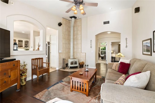 living room with a wood stove, ceiling fan, hardwood / wood-style floors, and a towering ceiling