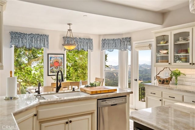 kitchen with stainless steel dishwasher, pendant lighting, light stone counters, and sink