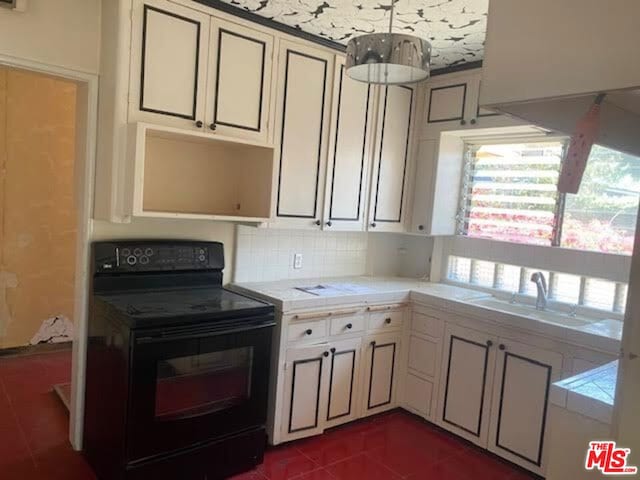 kitchen with decorative backsplash, black range with electric stovetop, dark tile patterned floors, tile counters, and sink