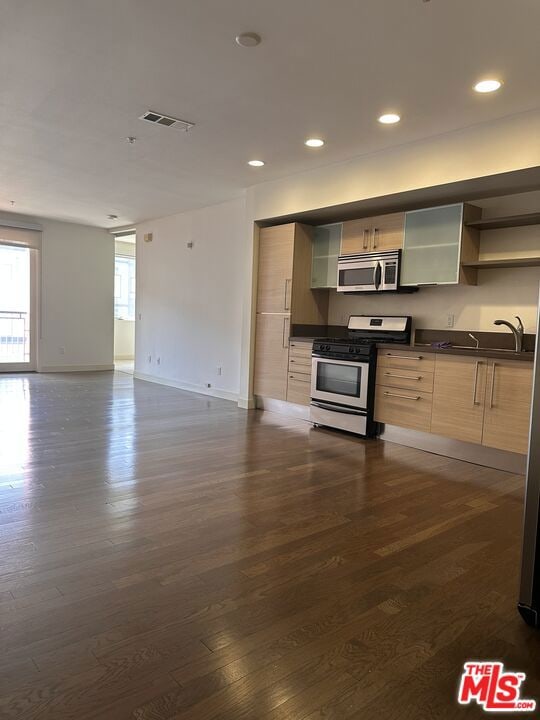 kitchen featuring light brown cabinetry, appliances with stainless steel finishes, dark wood-type flooring, and sink