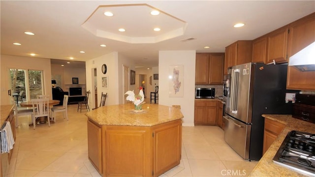 kitchen featuring a center island, a raised ceiling, light tile patterned floors, light stone counters, and stainless steel appliances