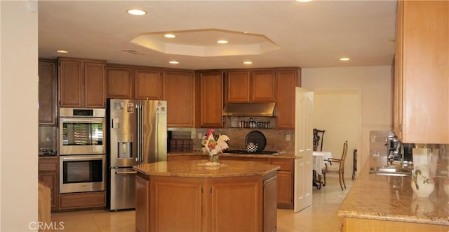 kitchen with a center island, light tile patterned floors, appliances with stainless steel finishes, a tray ceiling, and light stone counters