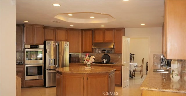 kitchen featuring stainless steel appliances, a tray ceiling, a center island, and light stone countertops