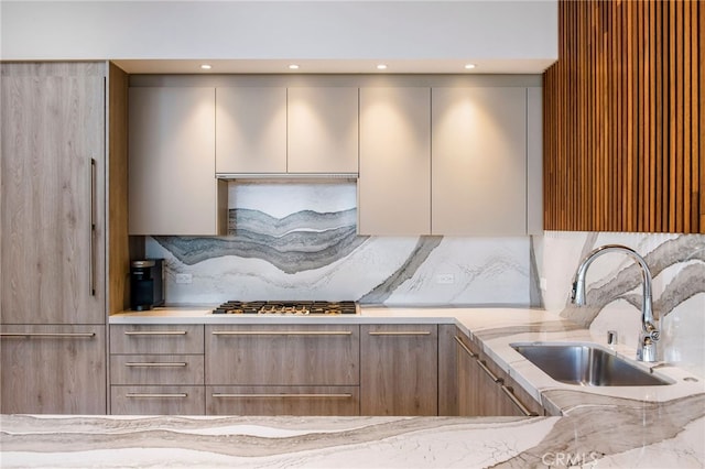 kitchen featuring stainless steel gas stovetop, sink, light stone counters, and decorative backsplash