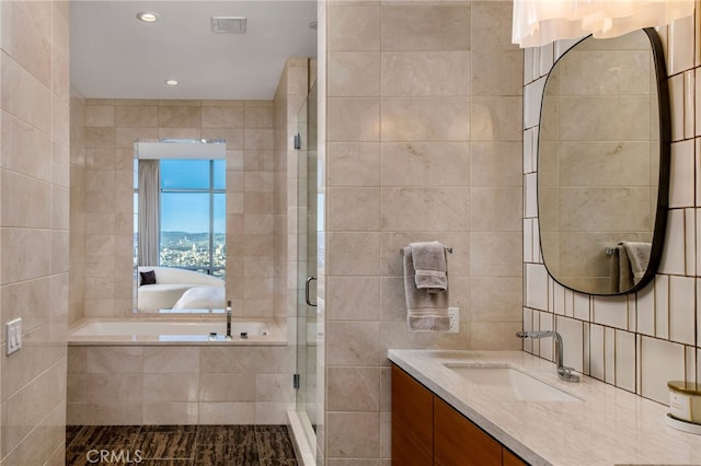 bathroom featuring plus walk in shower, tile walls, and vanity