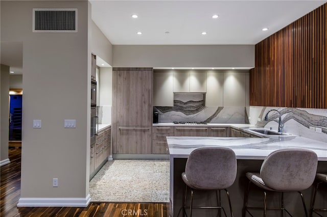 kitchen with sink, gas cooktop, kitchen peninsula, and a kitchen bar