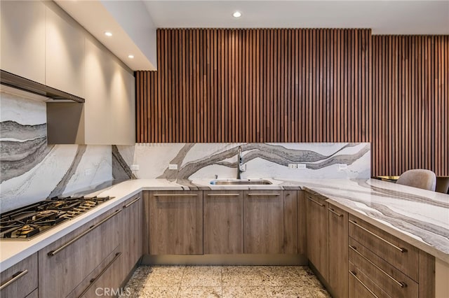 kitchen with stainless steel gas stovetop, light stone countertops, and sink