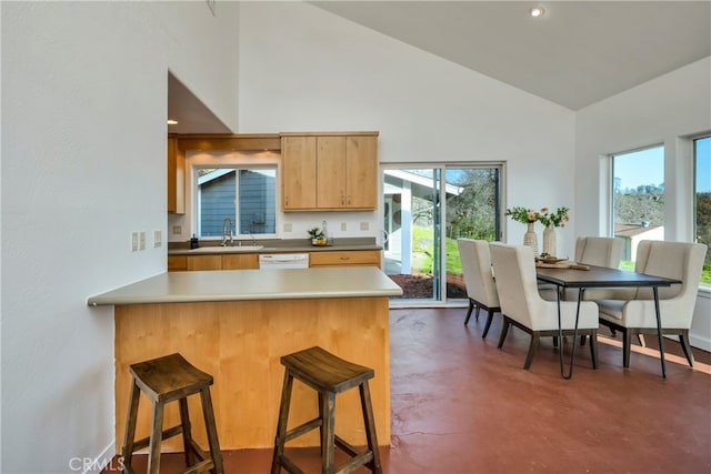 kitchen with kitchen peninsula, white dishwasher, a kitchen bar, vaulted ceiling, and sink