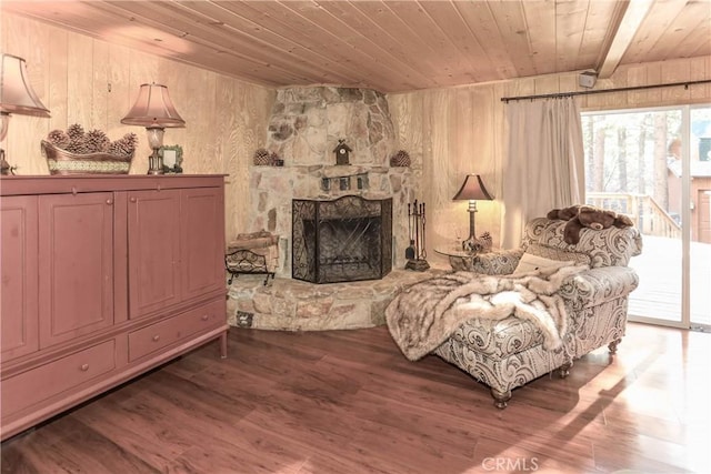 sitting room featuring wood ceiling, wooden walls, wood-type flooring, beamed ceiling, and a stone fireplace