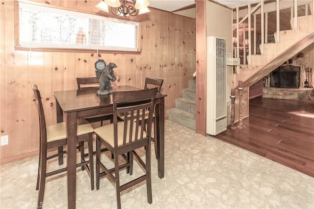 dining space featuring hardwood / wood-style floors, wood walls, a fireplace, and an inviting chandelier