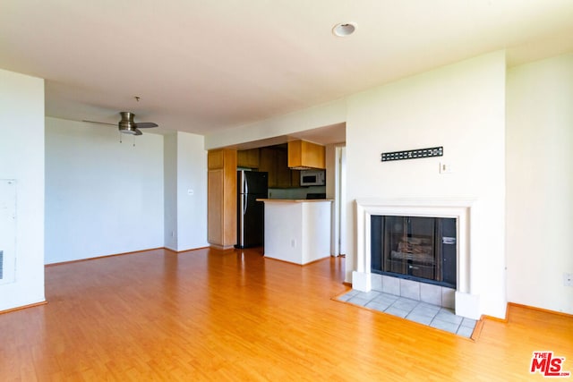 unfurnished living room featuring a tiled fireplace, light hardwood / wood-style floors, and ceiling fan