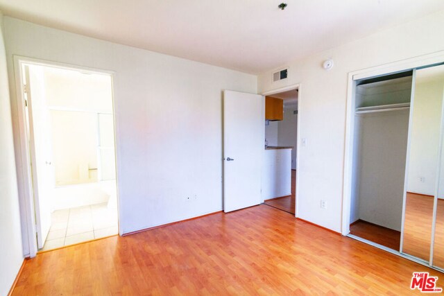 unfurnished bedroom featuring a closet, ensuite bathroom, and hardwood / wood-style flooring