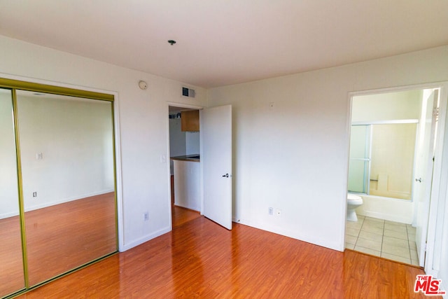 unfurnished bedroom with wood-type flooring, a closet, and ensuite bath